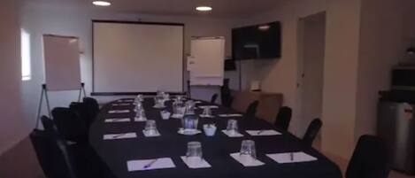 A conference room with a long table set for meetings, equipped with chairs, water glasses, and notepads.