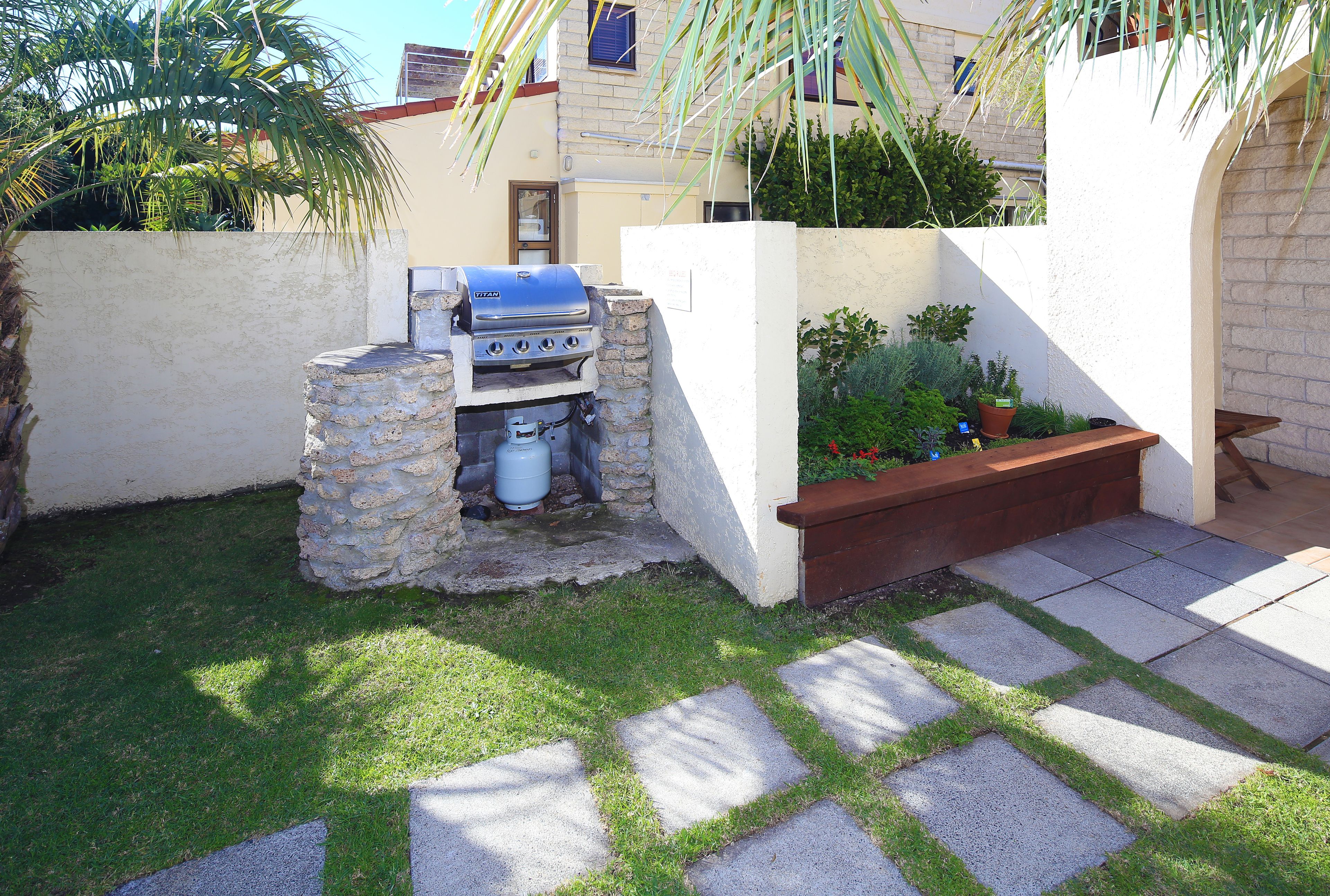 Ein Garten mit Steingrill, einem kleinen Pflanzenbeet und einem gepflasterten Weg.