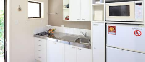 A modern kitchen with white cabinets, a sink, a microwave, and a refrigerator.