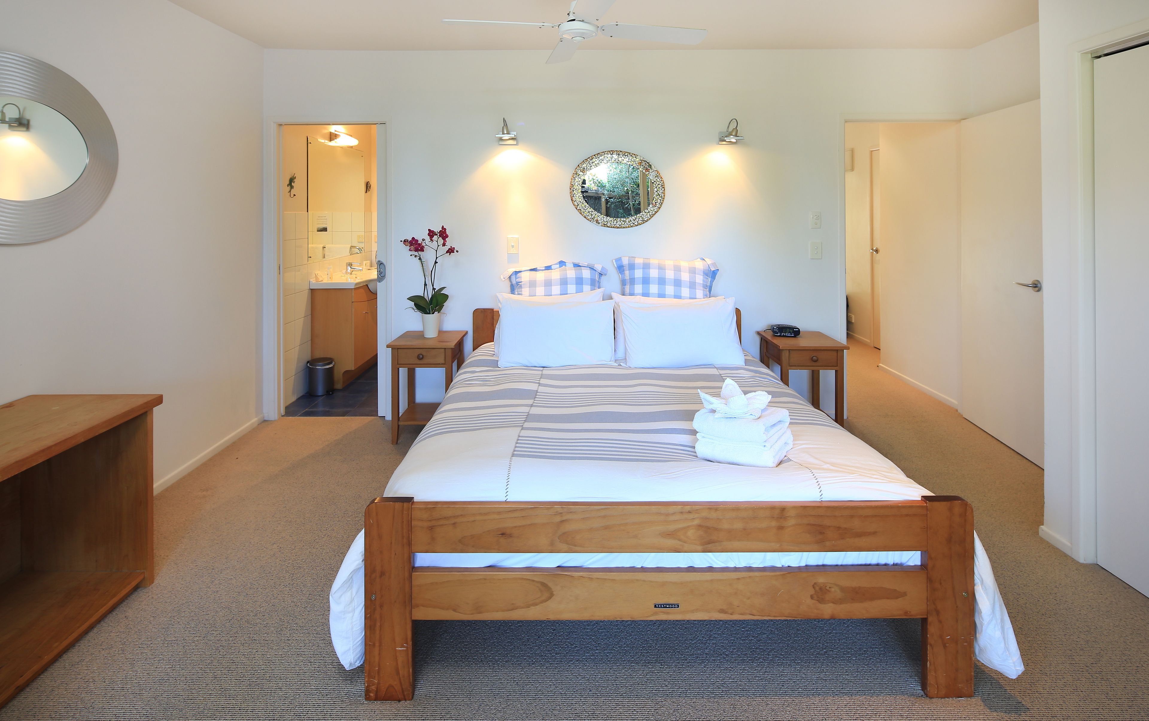 A neatly arranged bedroom with a wooden bed, bedside tables, a mirror, and a potted plant.