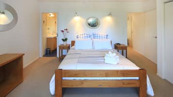 A neatly arranged bedroom with a wooden bed, bedside tables, a mirror, and a potted plant.
