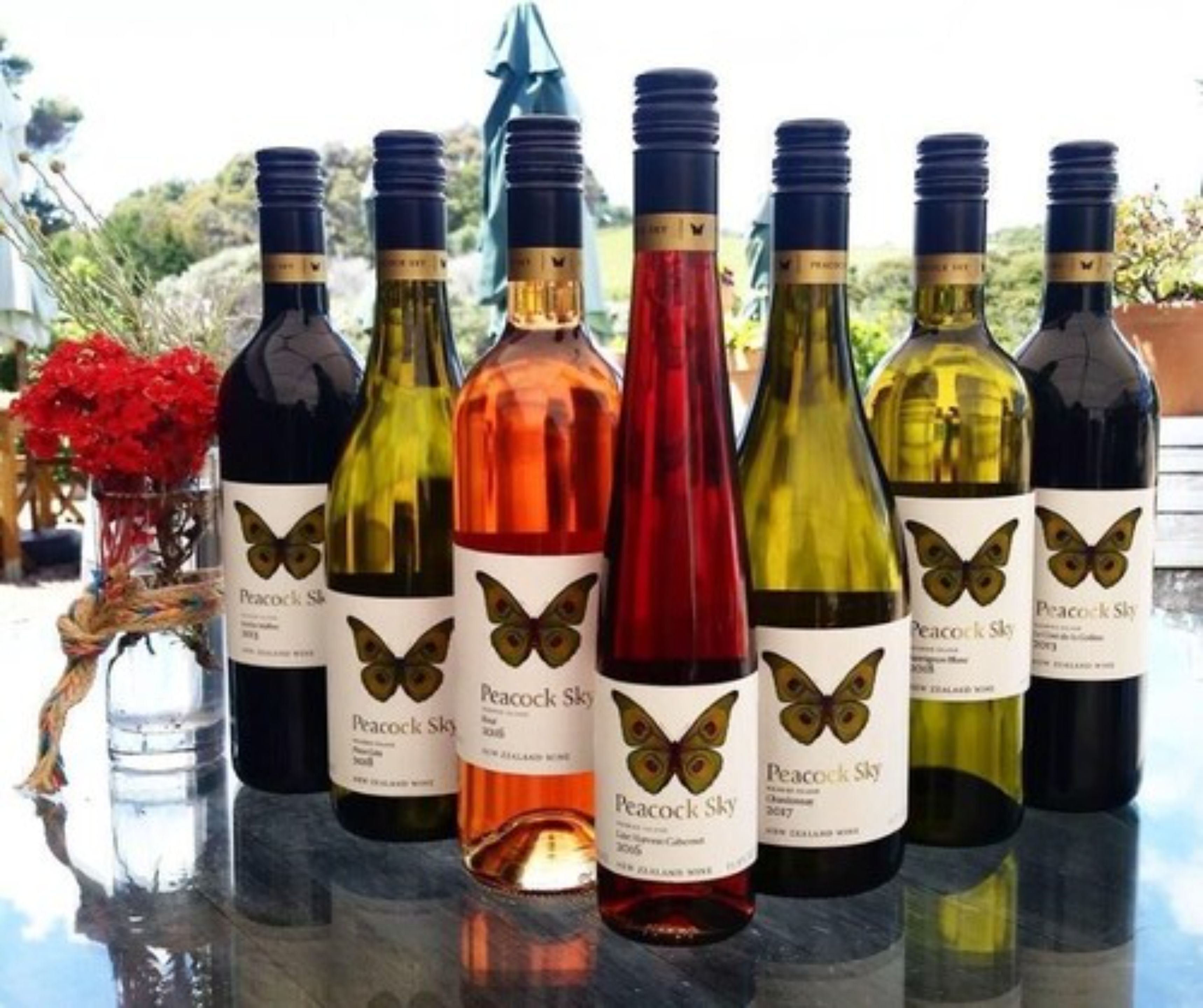 Une rangée de bouteilles de vin, dont les étiquettes représentent des papillons, est placée sur une surface réfléchissante.