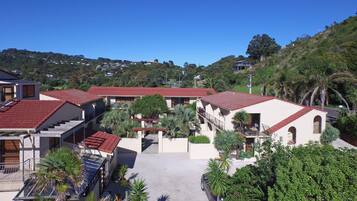 A residential area with multiple houses featuring red-tiled roofs, surrounded by lush greenery and hills in the background.