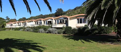 A row of modern villas with large windows, a well-maintained lawn, and a clear blue sky.