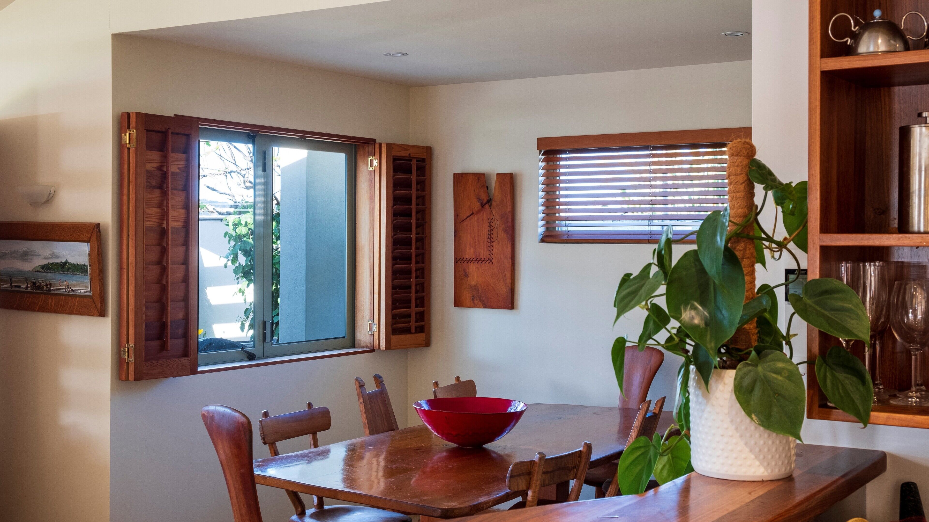 A dining area with a wooden table, chairs, a red bowl, and a potted plant.
