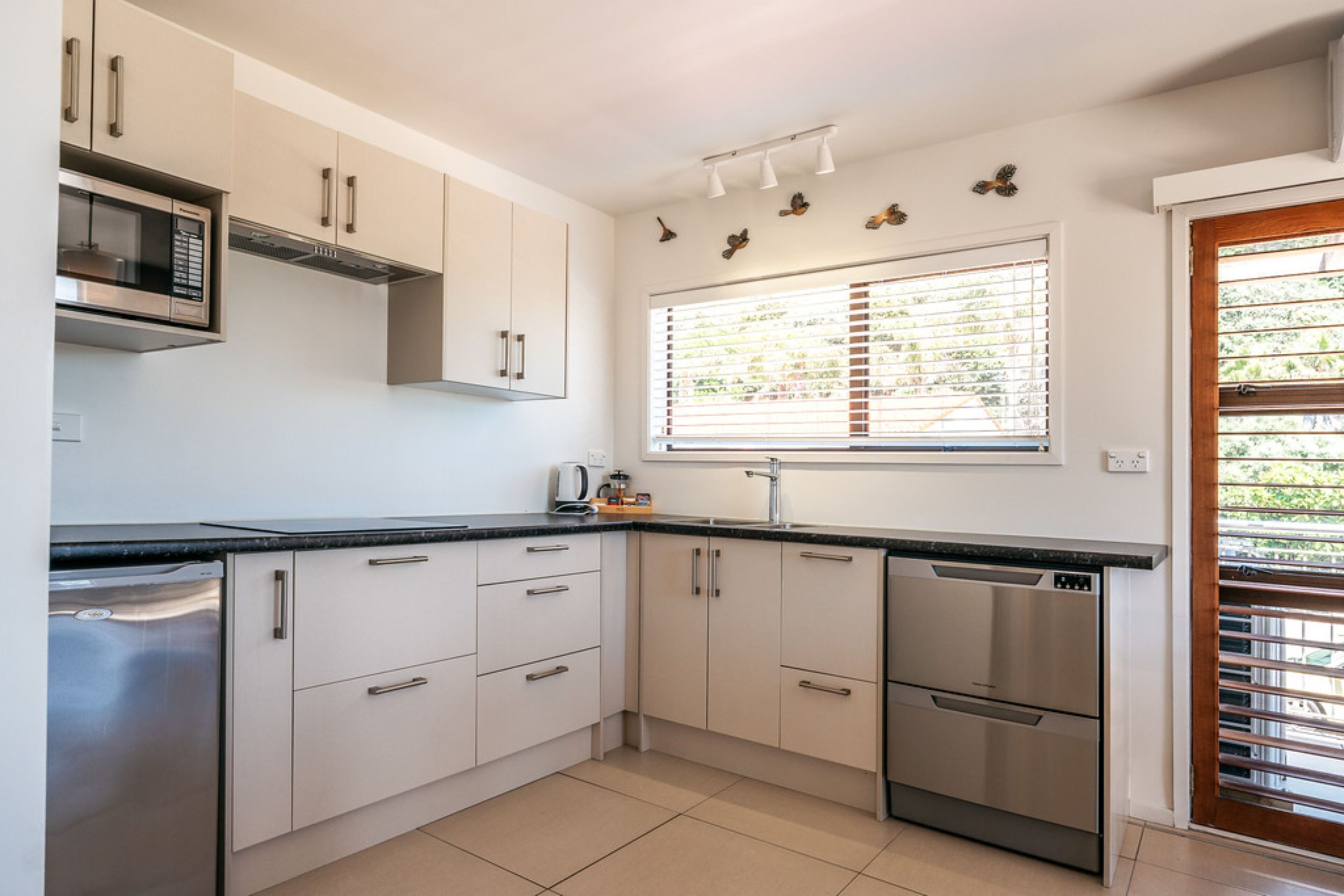 A modern kitchen with white cabinets, stainless steel appliances, and a window with blinds.