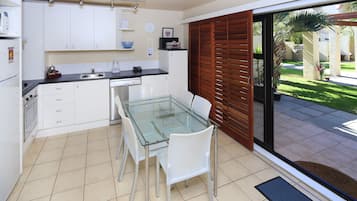 A modern kitchen with white cabinets, a glass dining table, and a sliding glass door leading to a patio.