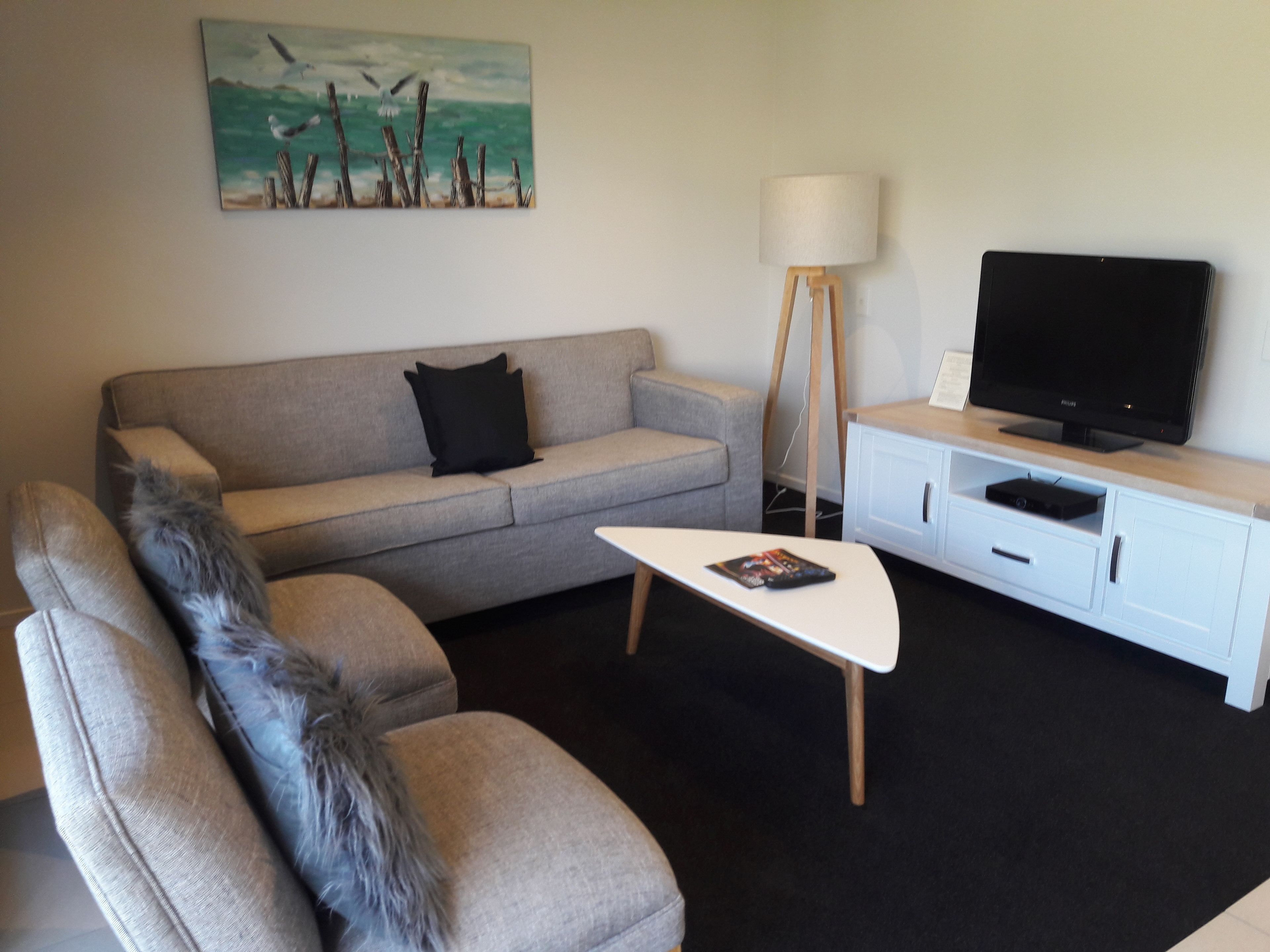 A living room with a grey sofa, a white coffee table, a television on a stand, and a painting of birds on the wall.