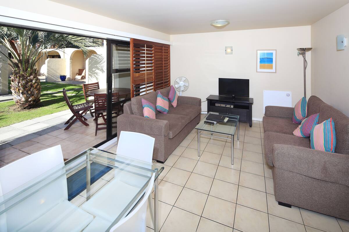 A living room with a glass table, two sofas, a TV, and a fan.