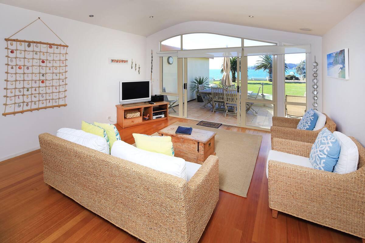 A spacious living area with wicker furniture, a flat-screen TV, and a view of the outdoors through large sliding doors.