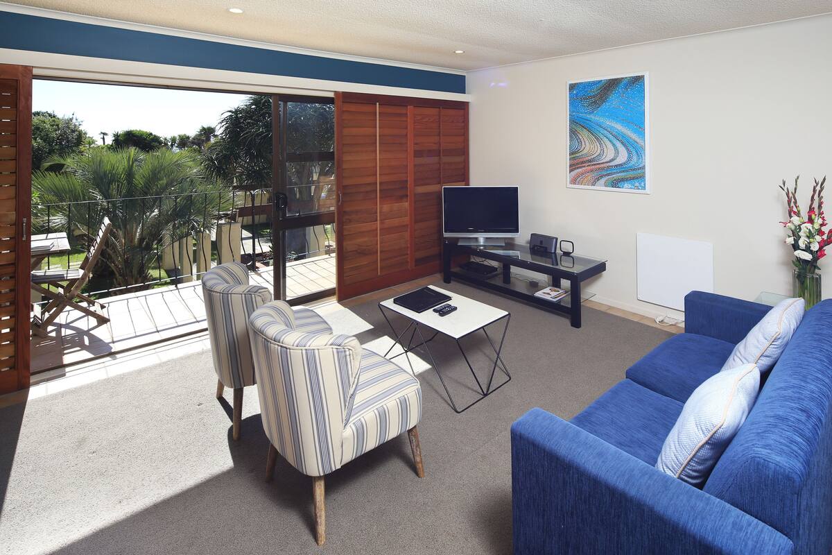 A living room with a blue sofa, striped armchair, and a TV on a stand.