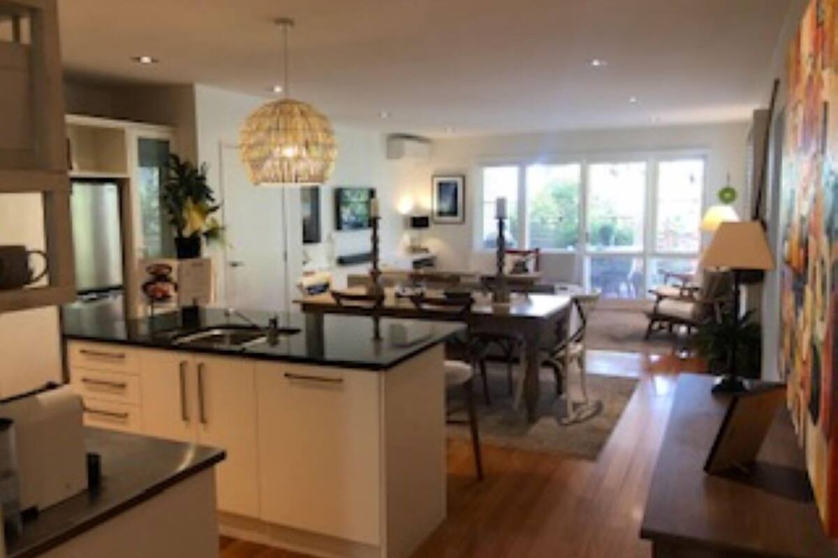 A modern kitchen with a central island, a dining area with a table and chairs, and a large window providing natural light.