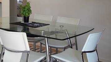 Un comedor con una mesa de vidrio rodeada de sillas blancas, una planta en maceta y un cuadro en la pared.