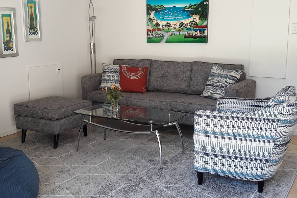 A living room with a grey sofa, a patterned armchair, a glass coffee table, and a floor lamp.