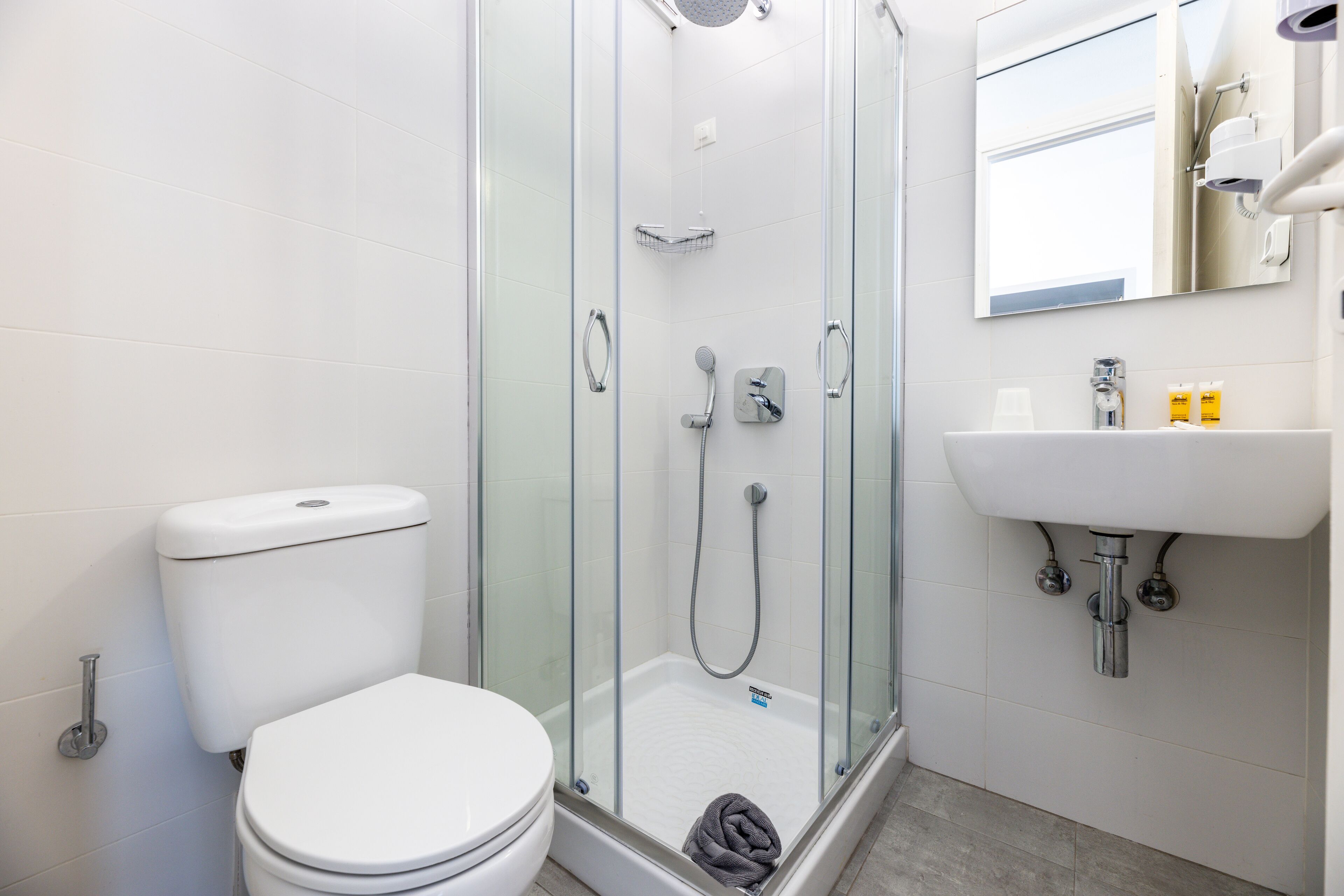 A modern bathroom with a glass-enclosed shower, a white toilet, and a sink with a mirror above it.