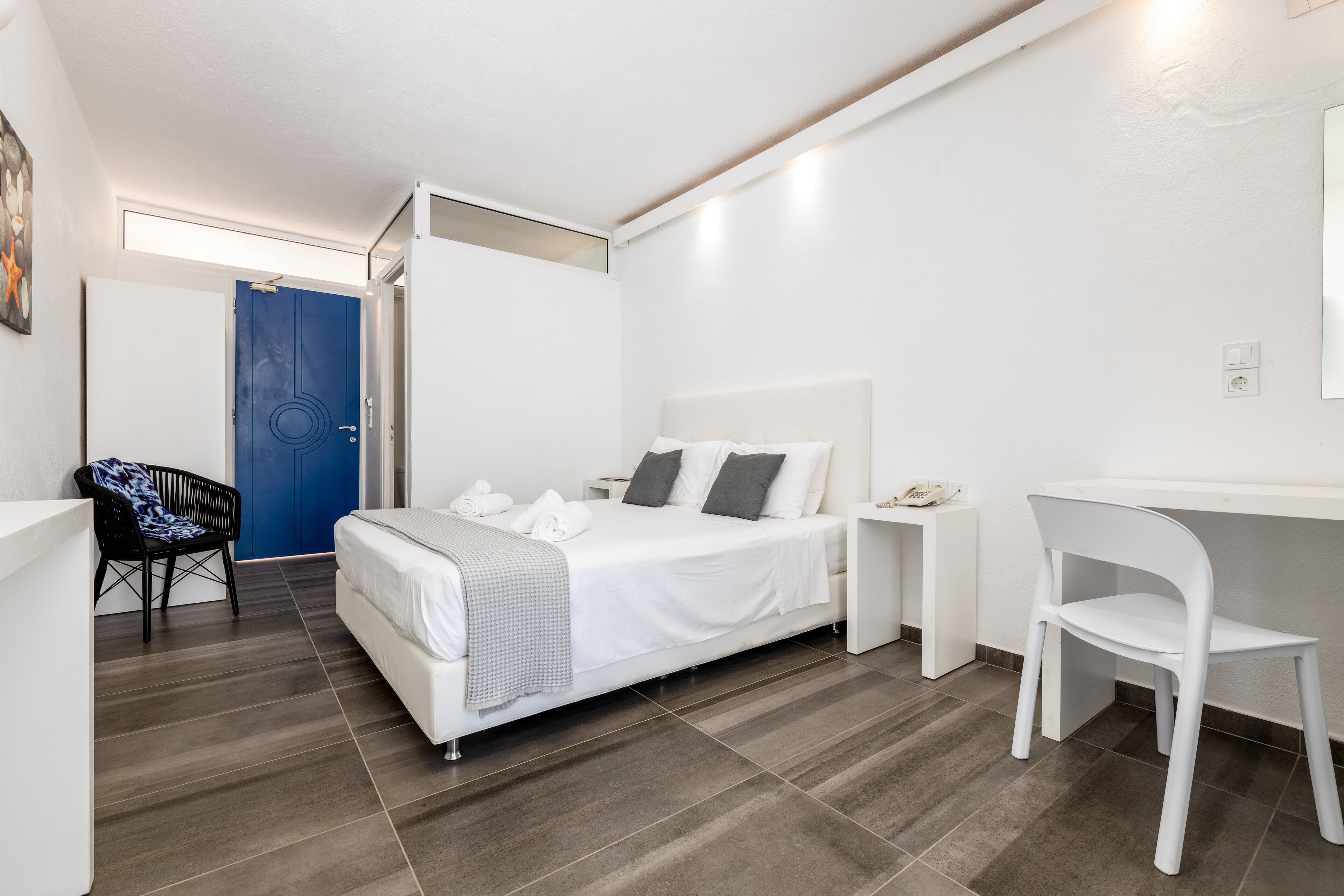 Moderni hotellihuone, jossa on sänky, työpöytä, tuoli ja sininen ovi.