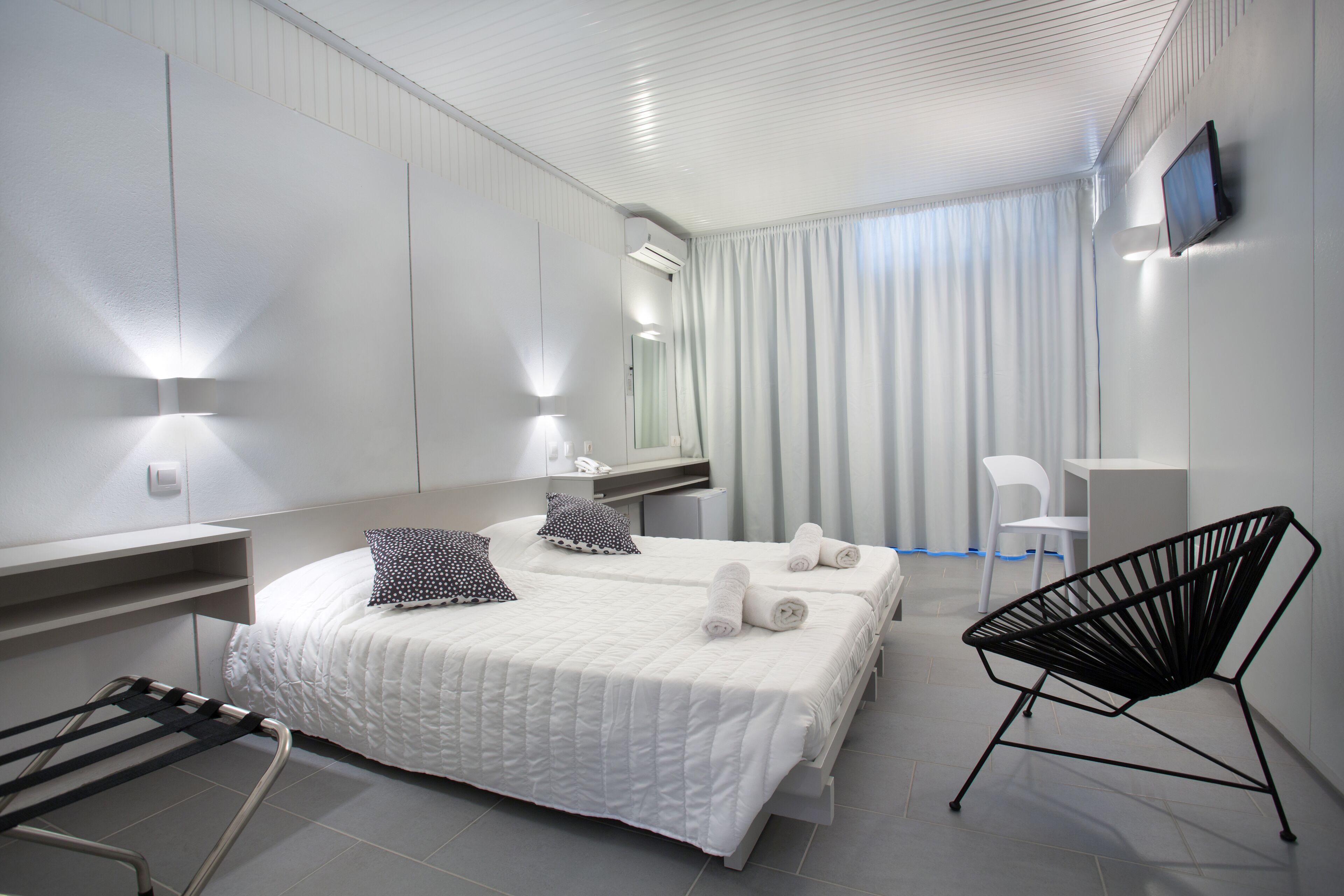 Una habitación de hotel moderna con una cama grande, un escritorio, una silla y un televisor en la pared.