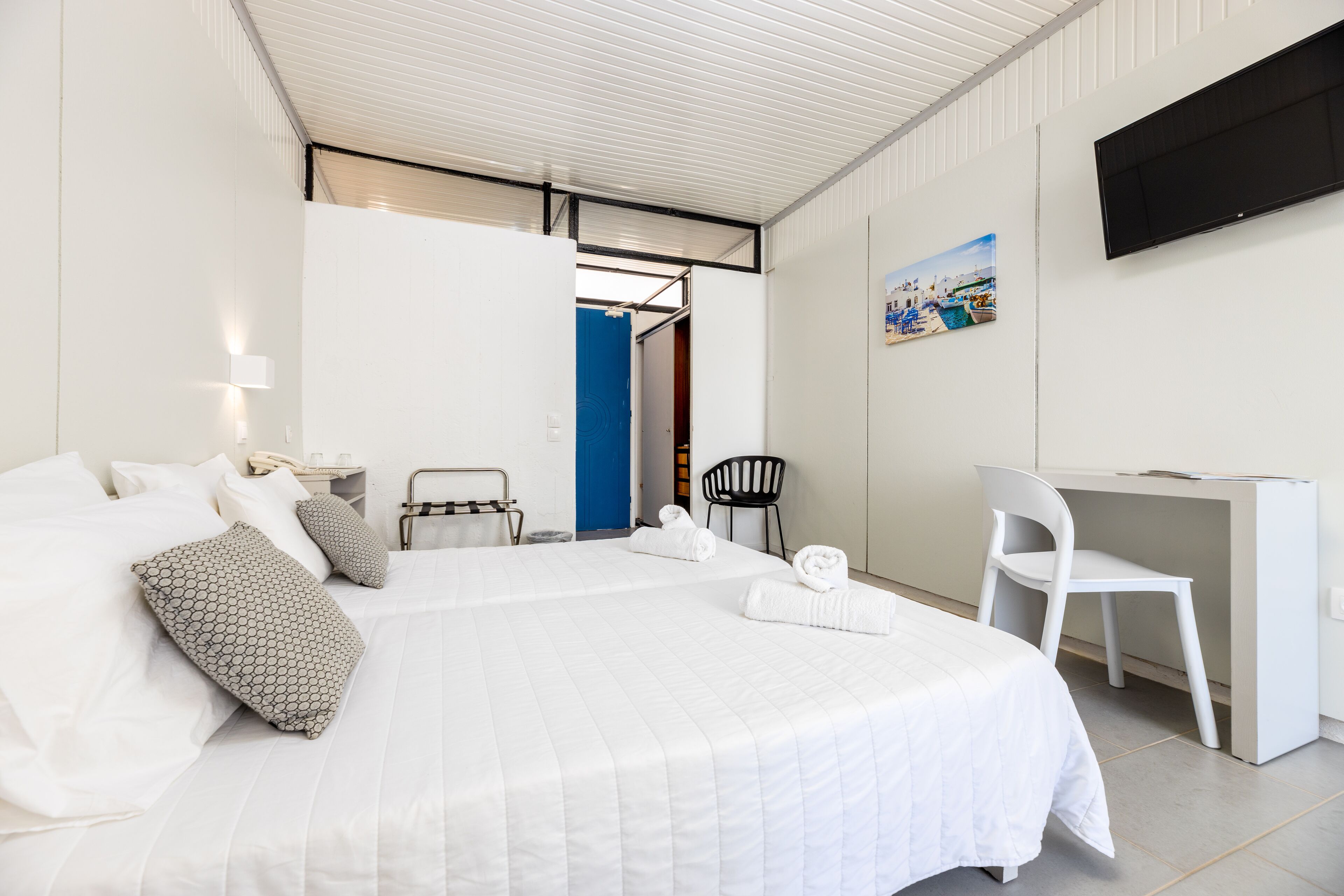 Habitación de hotel con cama, escritorio, silla, televisor y un cuadro en la pared.