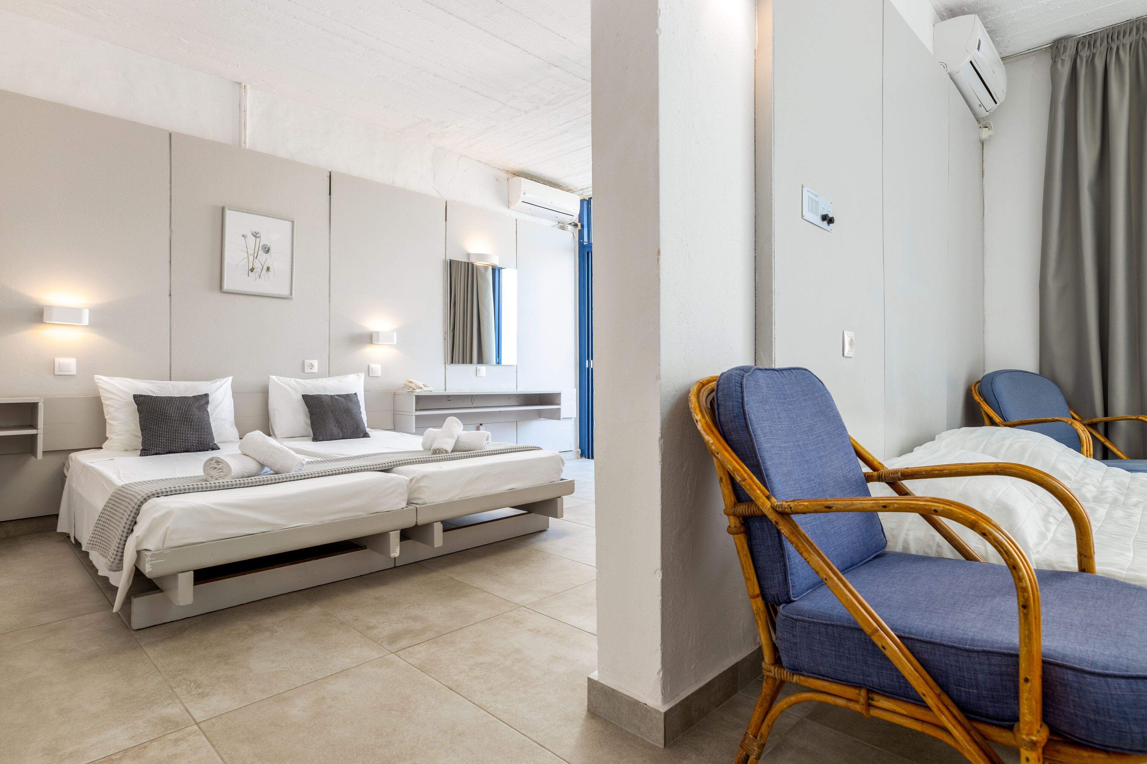 Une chambre d’hôtel moderne équipée d’un lit, de deux chaises, d’une table de chevet et d’un climatiseur fixé au mur.
