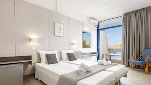 Una habitación de hotel moderna con dos camas, una kitchenette pequeña, un balcón con vistas y una silla de mimbre.