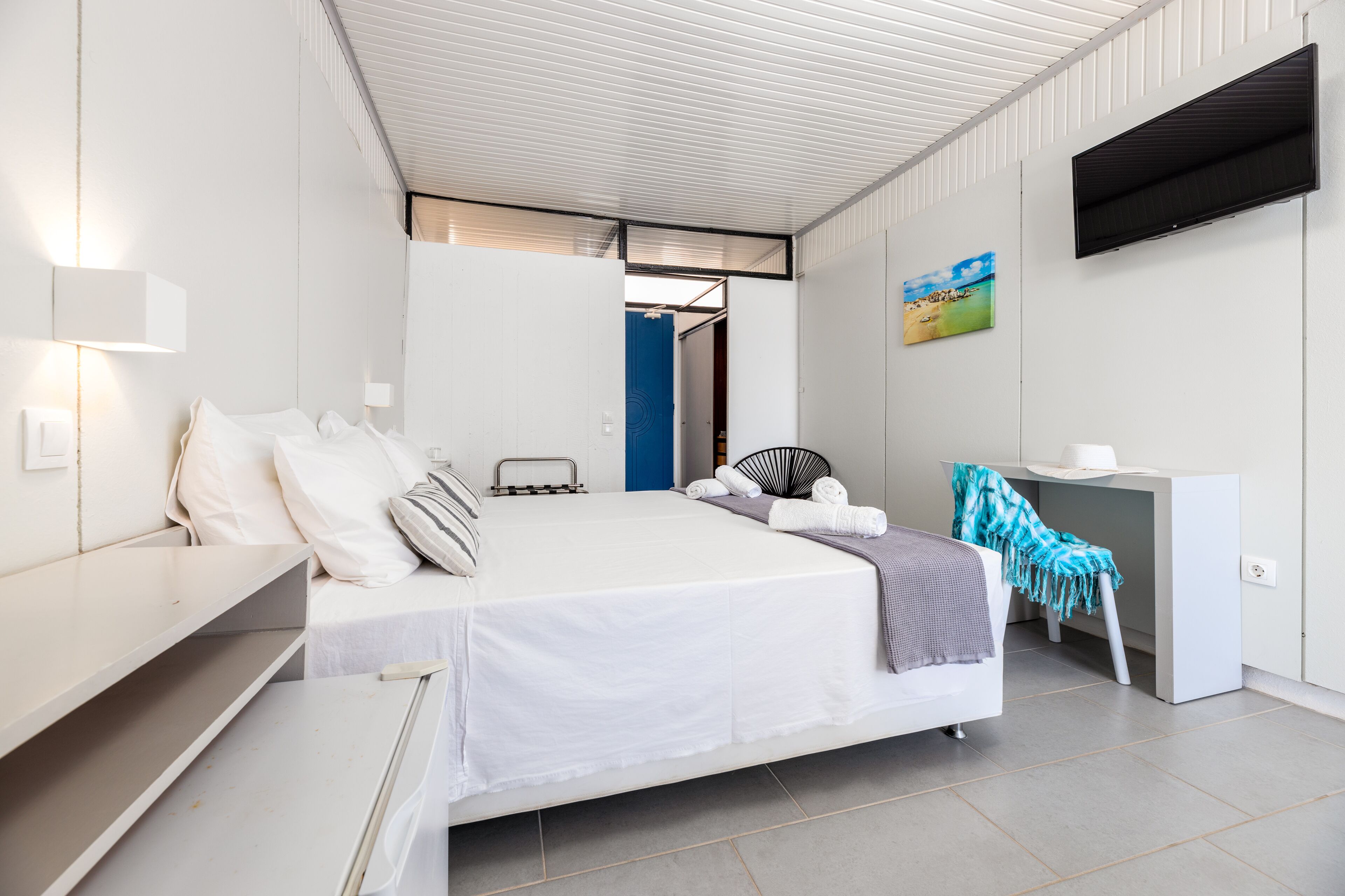 Een moderne hotelkamer met een bed, een bureau, een stoel en een aan de muur bevestigde televisie.