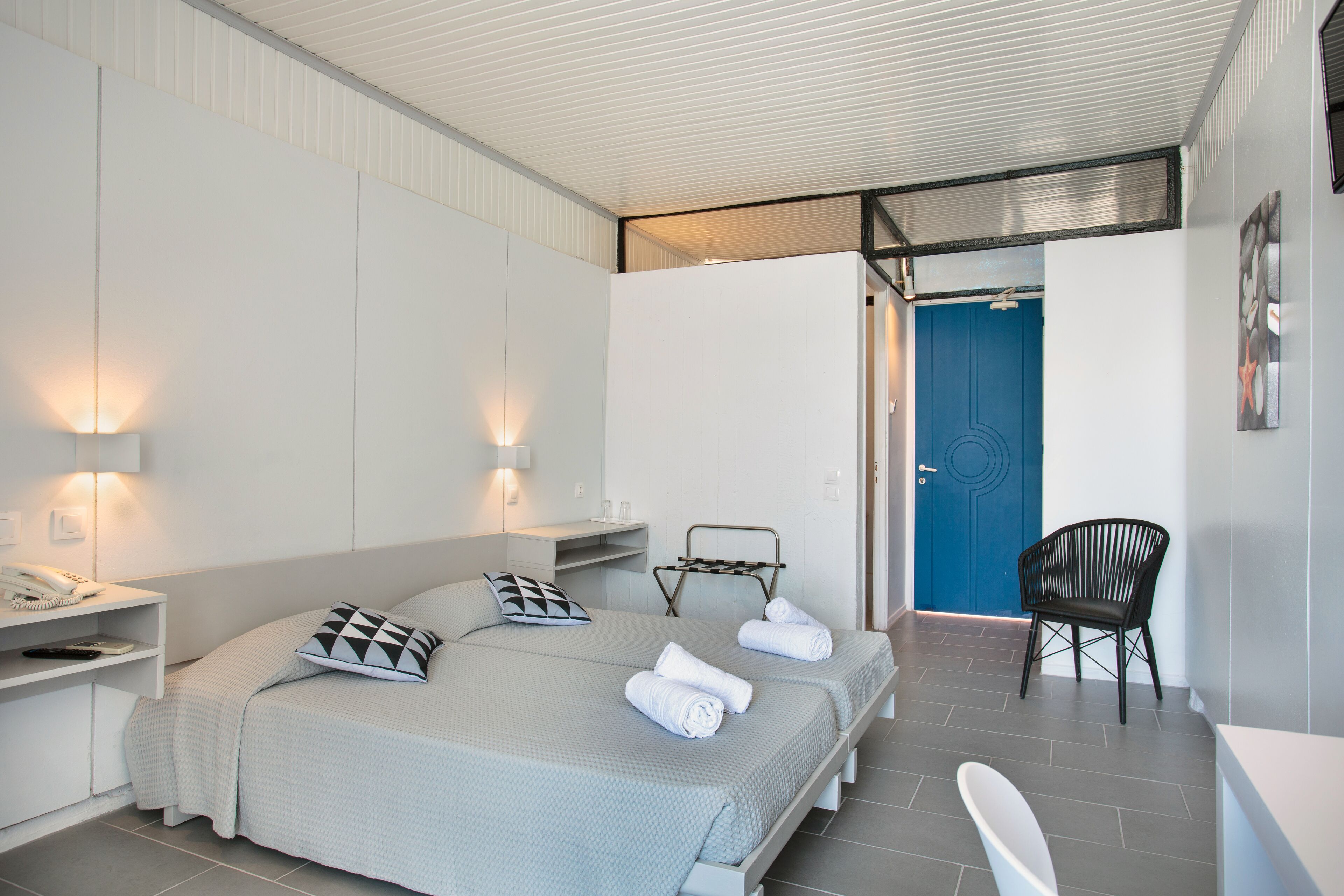 A modern hotel room with a bed, bedside tables, a chair, and a bathroom visible through an open door.
