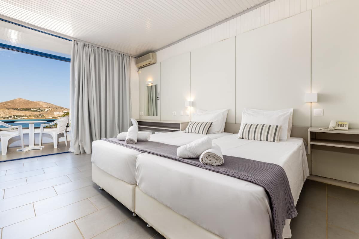 A hotel room with a large bed, a bedside table, a lamp, and a view of a mountainous landscape.