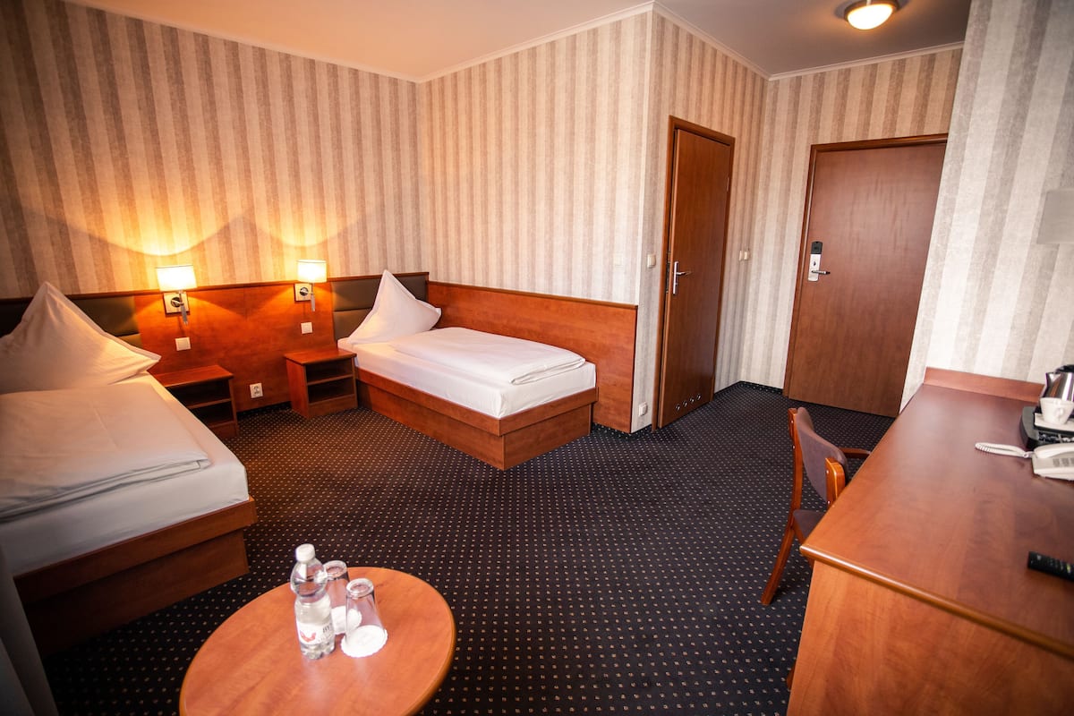 Hotellihuone, jossa on sänky, yöpöydät, työpöytä, tuoli ja pyöreä pöytä, jonka päällä on pulloja.