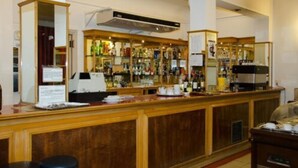 A bar area with a wooden counter, shelves of bottles, and a coffee machine. - Grand Hotel Balbi (Mendoza)