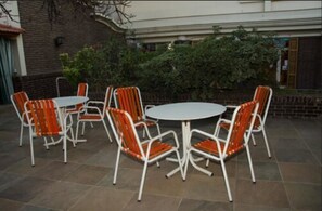 An outdoor patio with a round table and six orange and white chairs. - Grand Hotel Balbi (Mendoza)