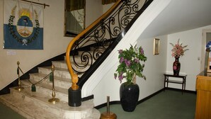 A marble staircase with a black handrail and golden stanchions, leading to a landing with a large black vase and potted plants. - Grand Hotel Balbi (Mendoza)
