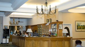A reception area with a wooden counter, chandeliers, and a clock on the wall. - Grand Hotel Balbi (Mendoza)