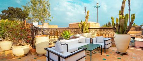A rooftop terrace with outdoor seating, potted plants, and a clear view of the sky.