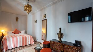 A hotel room with a bed, a television, a dresser, and a lamp.