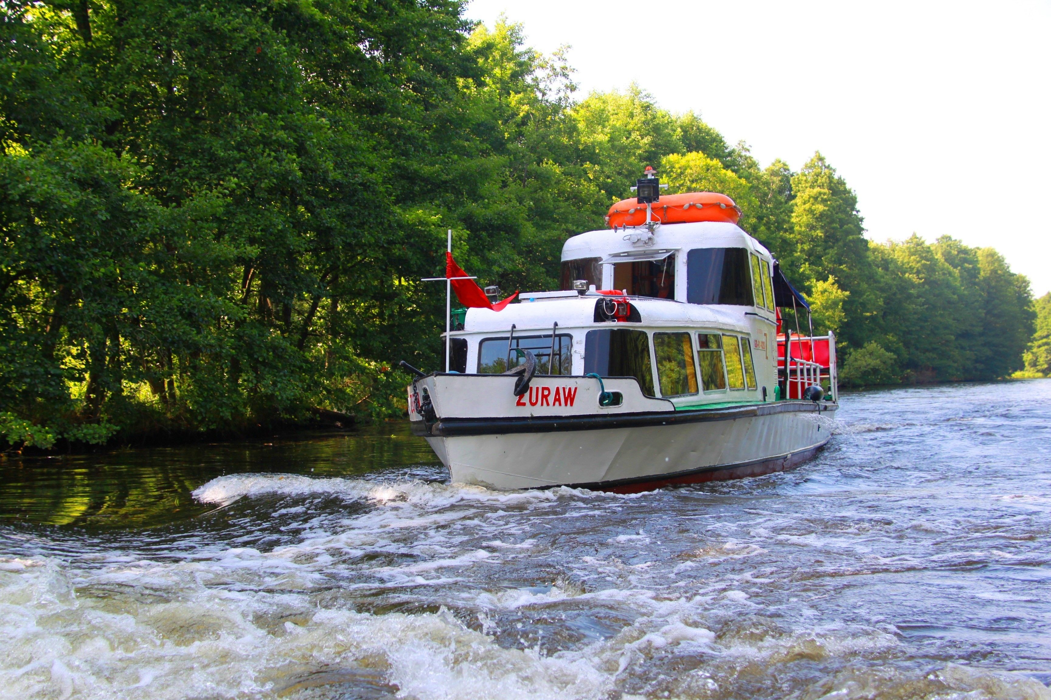 A boat named ZURAW on a river surrounded by dense green foliage.