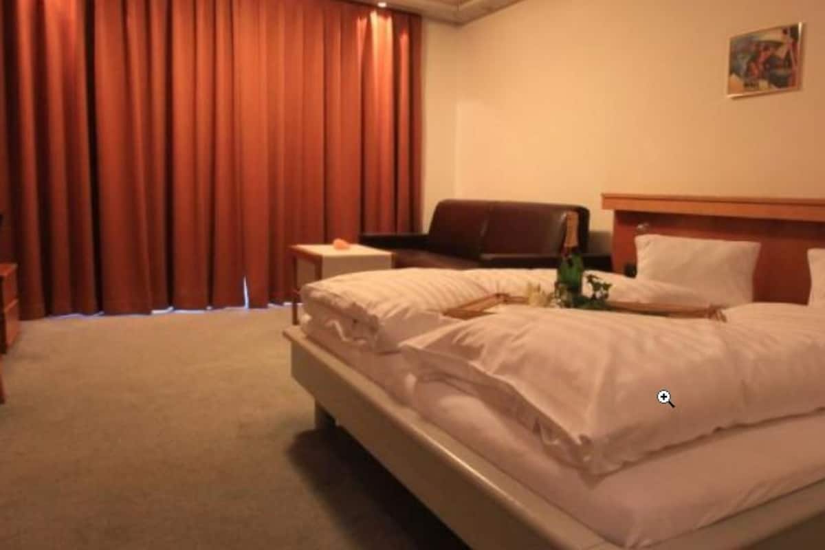 Una habitación de hotel con cama, escritorio, silla, televisor y ventana con cortinas.