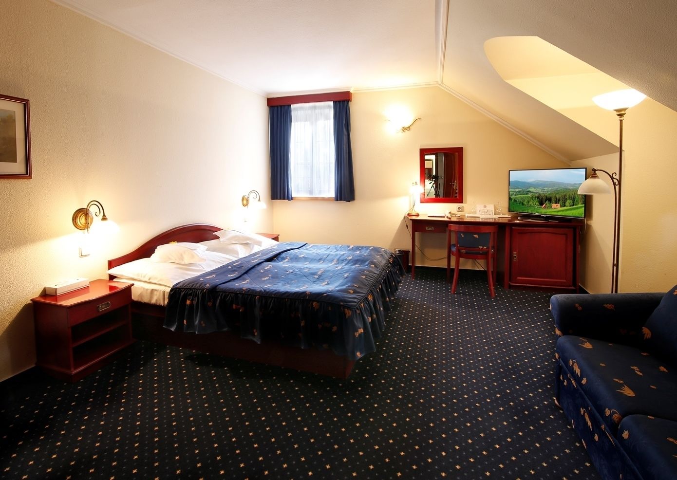 A hotel room with a bed, a desk, a chair, a TV, and a lamp.