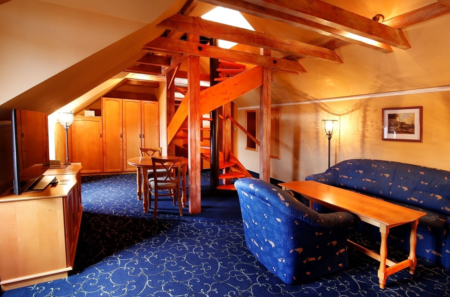 A cozy room with a wooden staircase, a blue patterned sofa, and a dining table with chairs.