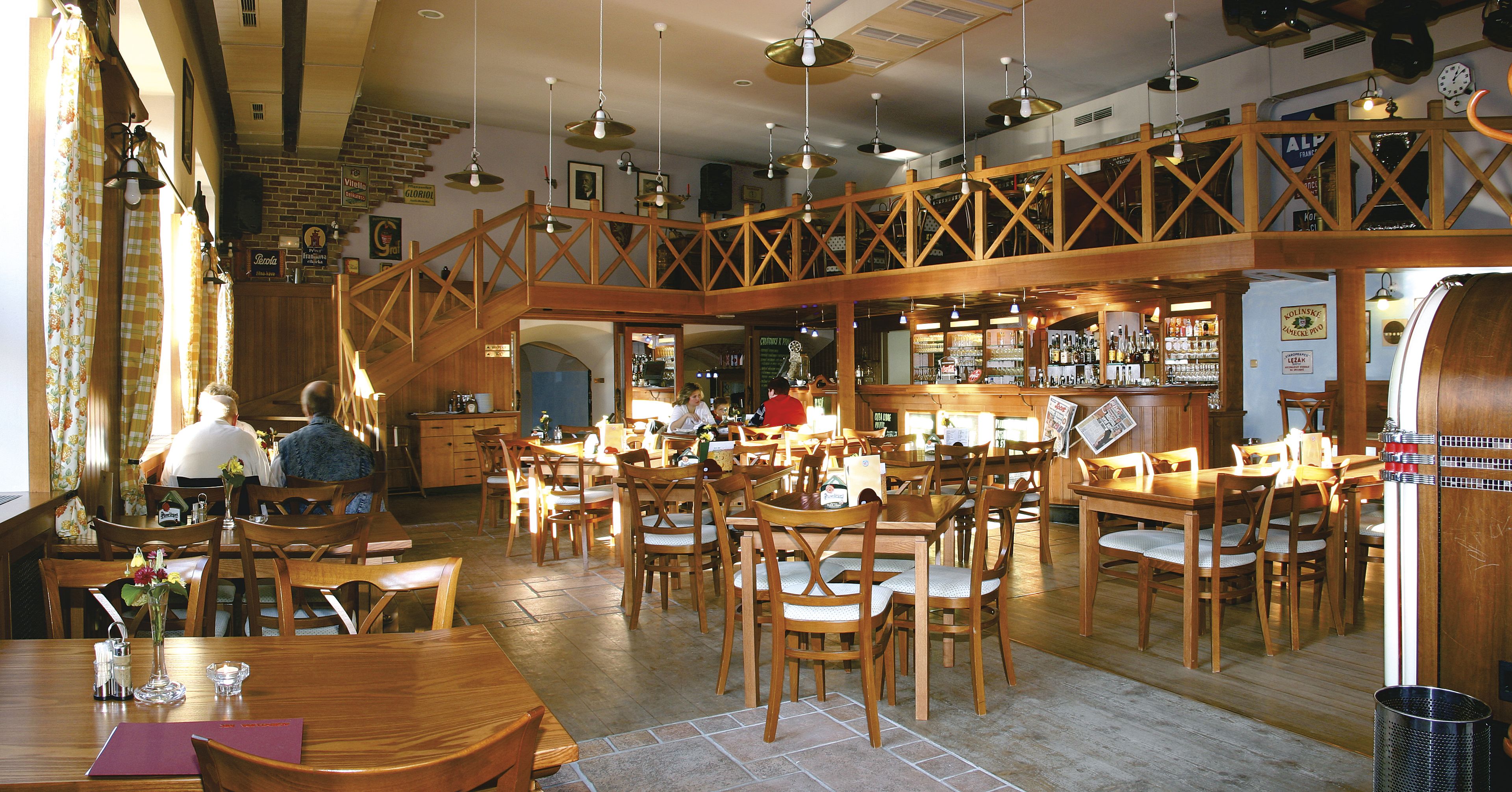 A spacious restaurant with wooden furniture, a bar area, and a staircase leading to an upper level.