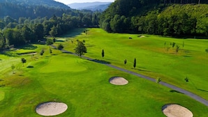 An aerial view of a golf course with multiple sand bunkers, a winding path, and a backdrop of dense forest and hills. - Agh Hotel (Roznov Pod Radhostem)