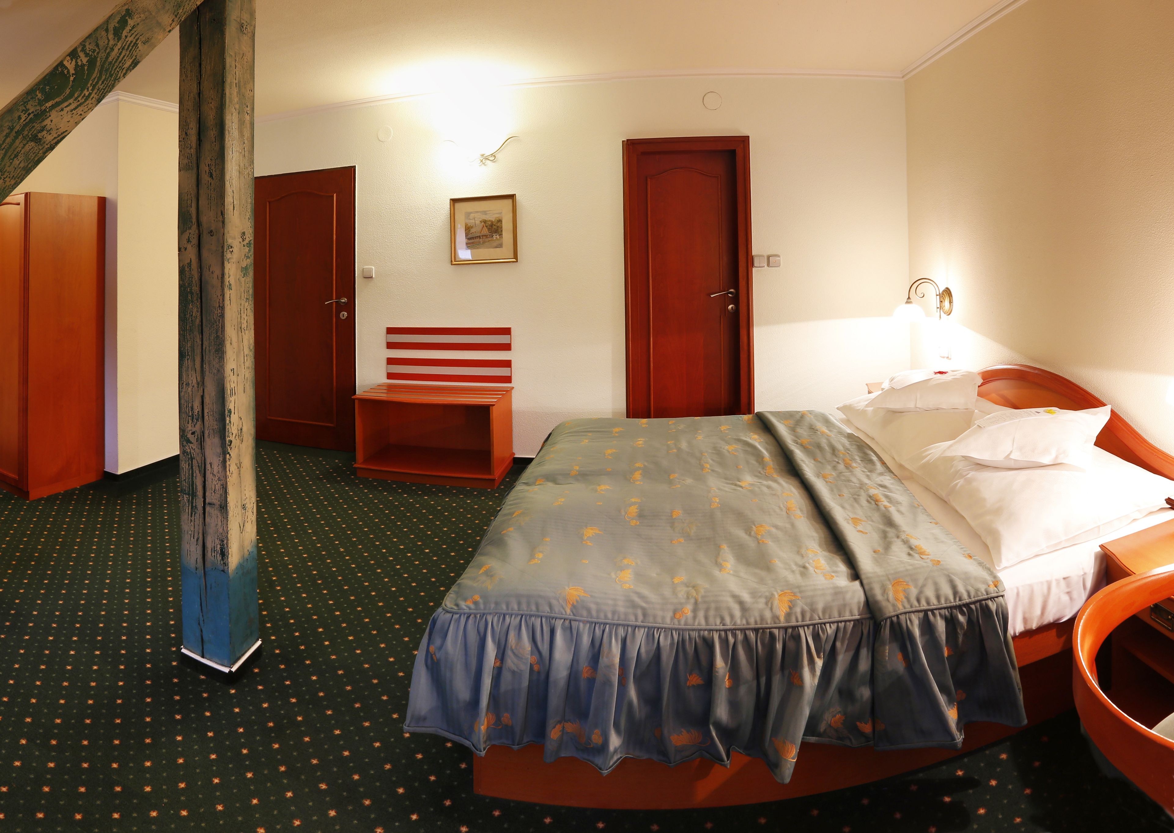 A hotel room with a bed, a wooden bench, a door, and a wall-mounted light fixture.