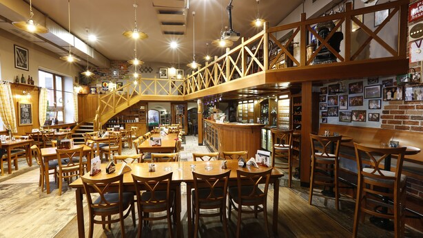 A restaurant with wooden tables and chairs, a bar area, and a staircase leading to an upper level. - Agh Hotel (Roznov Pod Radhostem)