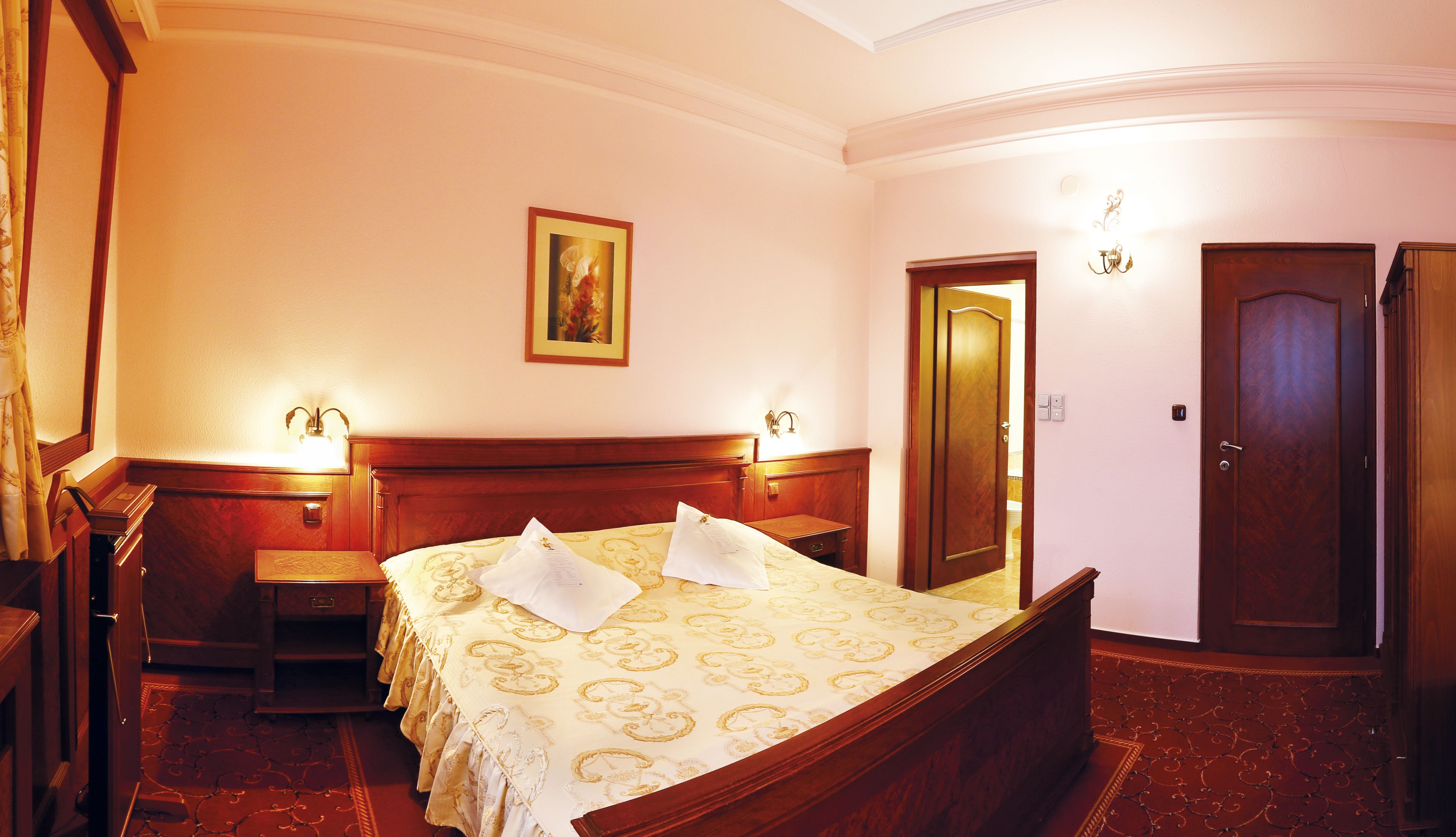 A hotel room with a wooden bed, two bedside tables, a nightstand, a painting on the wall, and a door.