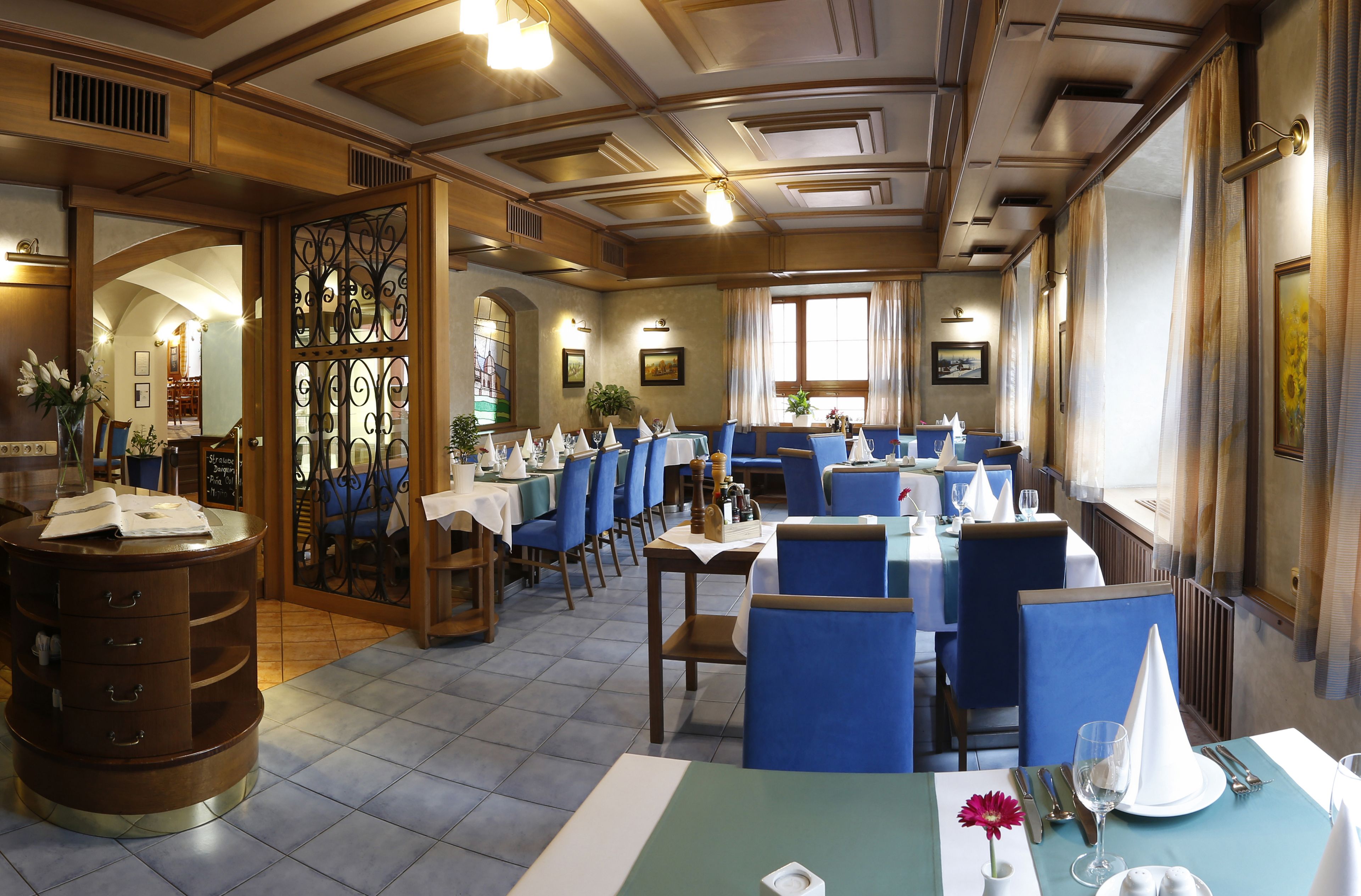 A restaurant with blue upholstered chairs, wooden tables, and a decorative iron partition.