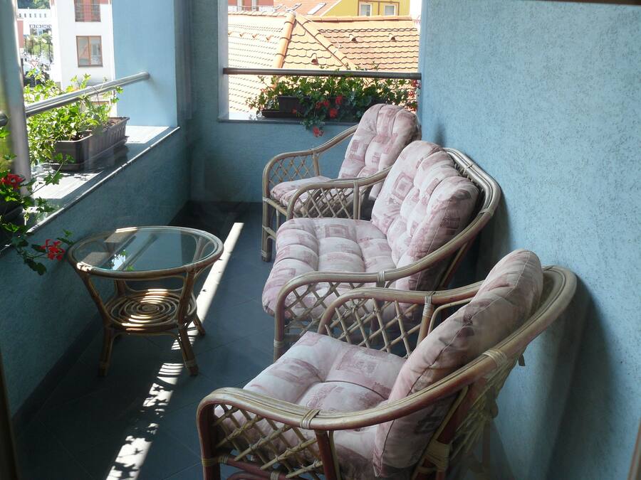 A balcony with wicker chairs and a glass table, a potted plant, and a view of buildings in the background.