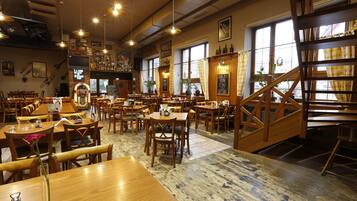 Un restaurante con mesas y sillas de madera, una escalera y ventanas grandes.