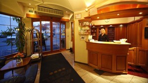A hotel lobby with a reception desk, a large window, a plant, and a seating area. - Agh Hotel (Roznov Pod Radhostem)