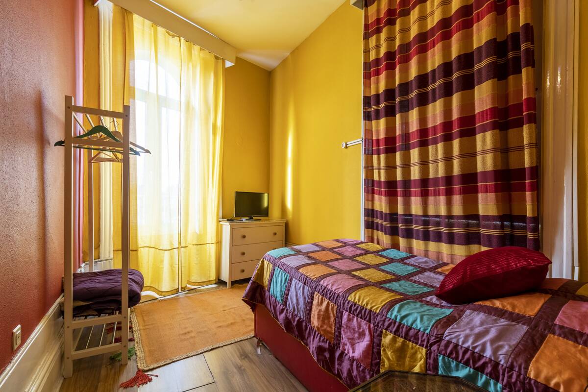 A bedroom with a bed, a dresser, a TV, and a window with curtains.