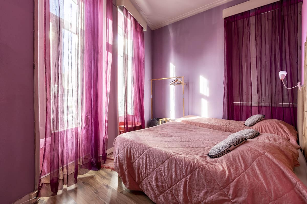 A bedroom with two beds, purple walls, and sheer curtains.
