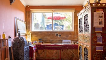 Um quarto com janela, pia, armário e mesa coberta por um tecido vermelho.